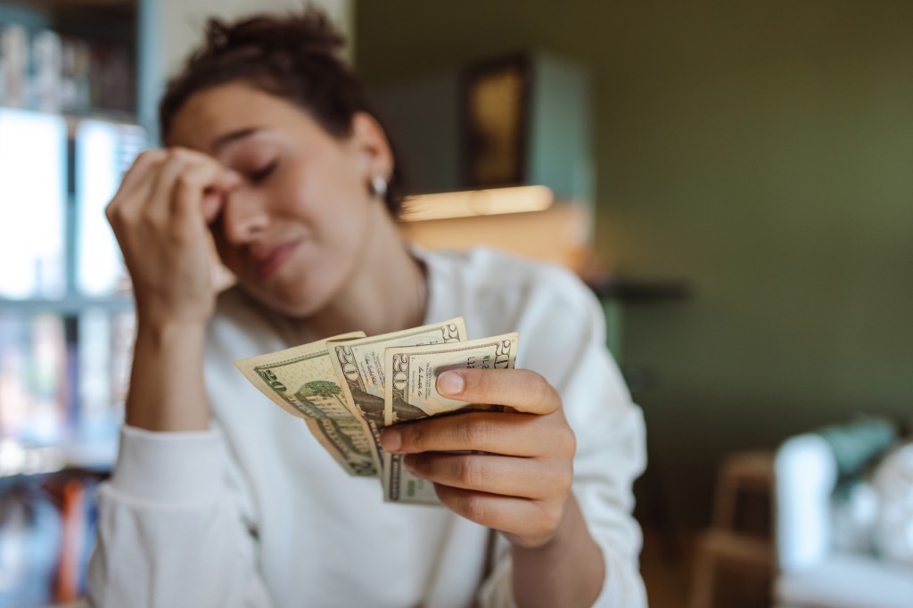 Worried young woman counting money on a table in her living room